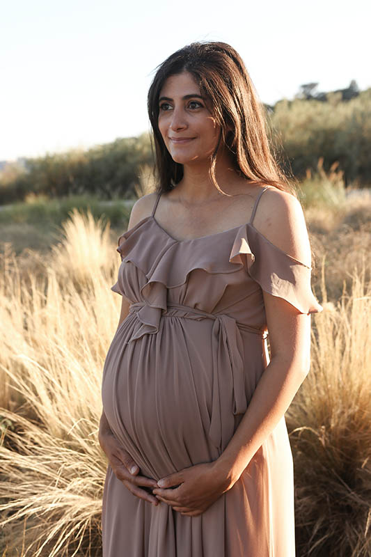 Femme enceinte devant des herbes hautes au soleil couchant